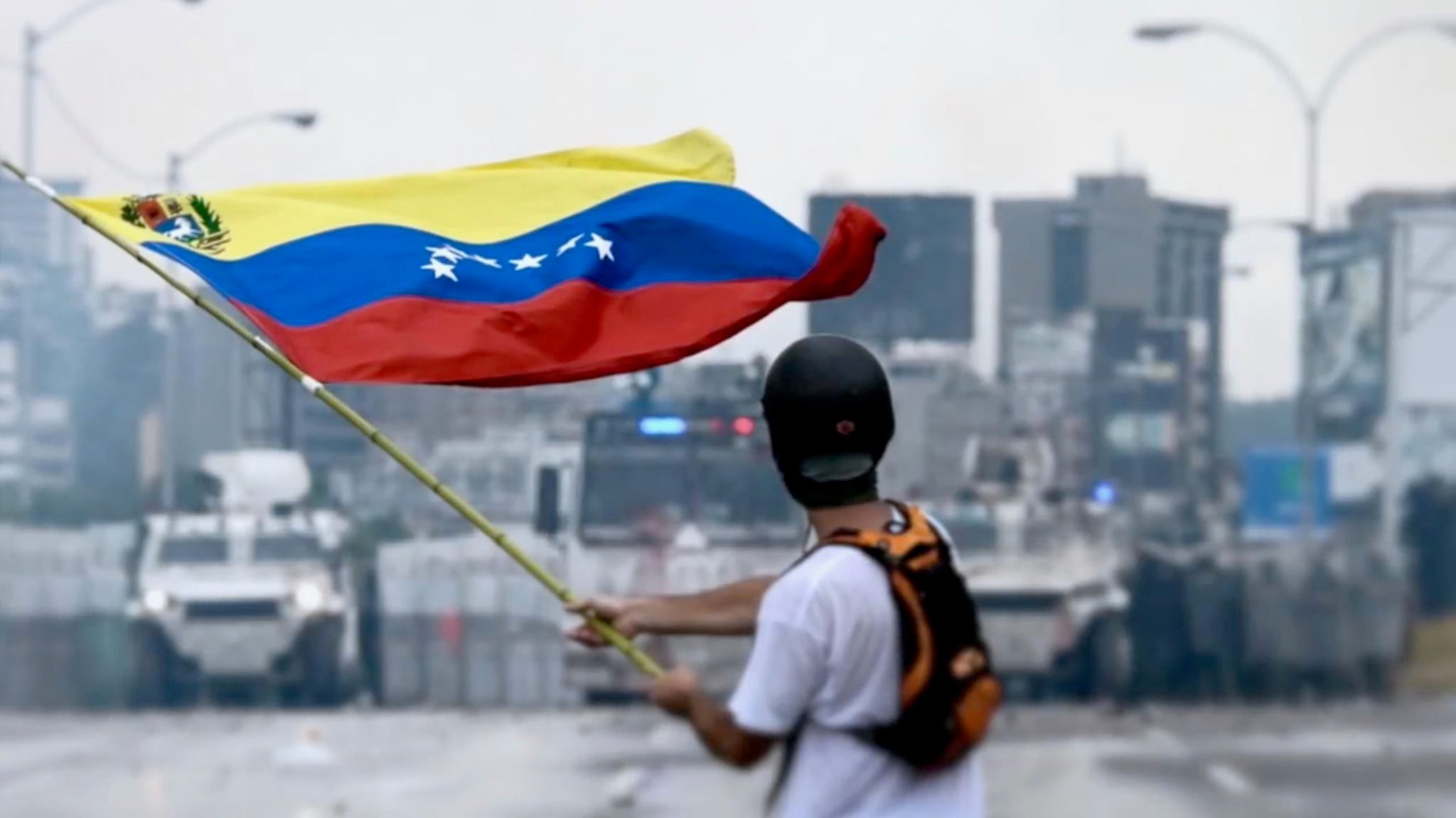 <p>A protestor facing Venezuela’s national guard in May 2017 (image: <a href="https://commons.wikimedia.org/wiki/File:2017_Venezuelan_protests_flag.jpg" target="_blank" rel="noopener">Efecto Eco </a>)</p>