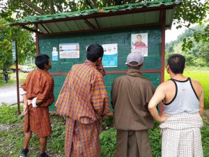 <p>Bhutanese scrutinise claims on an election board &#8211; the only place where political parties are allowed to put promotional material [image courtesy: Kuensel]</p>