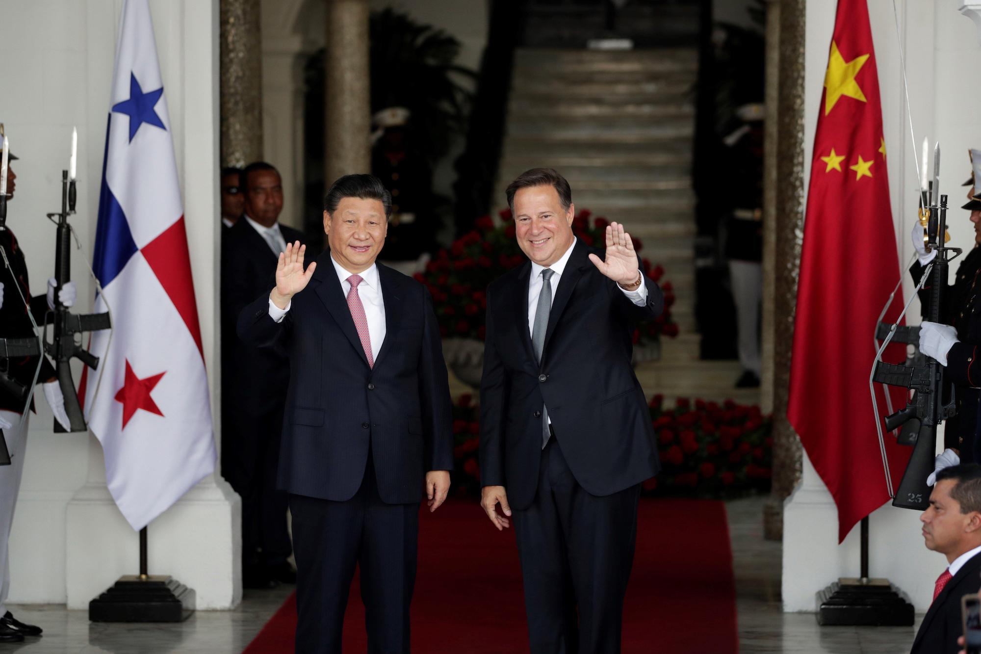 Juan Carlos Varela e Xi Jinping se cumprimentam, com as bandeiras do Panamá e da China de cada lado.
