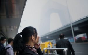 woman looks over air pollution in Beijing while wearing a mask