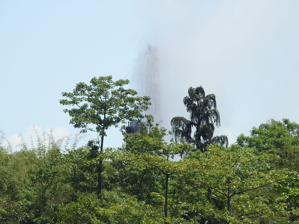 The rig spewing out gas through some trees, three days after the blowout [image by: Binanda Hatibaruah]