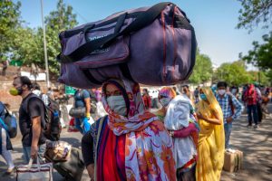 Indians wearing protective masks stand with their luggage in queue outside a railway station [image: Alamy]