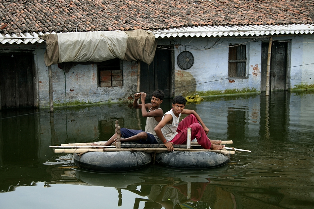 two boys float on tyres and wood across the water.  Much of Patna, the capital of Bihar, was flooded for over a fortnight last year [image by: Louise Batalla Duran/Alamy]