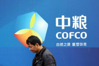 a Chinese man standing next to a Cofco poster