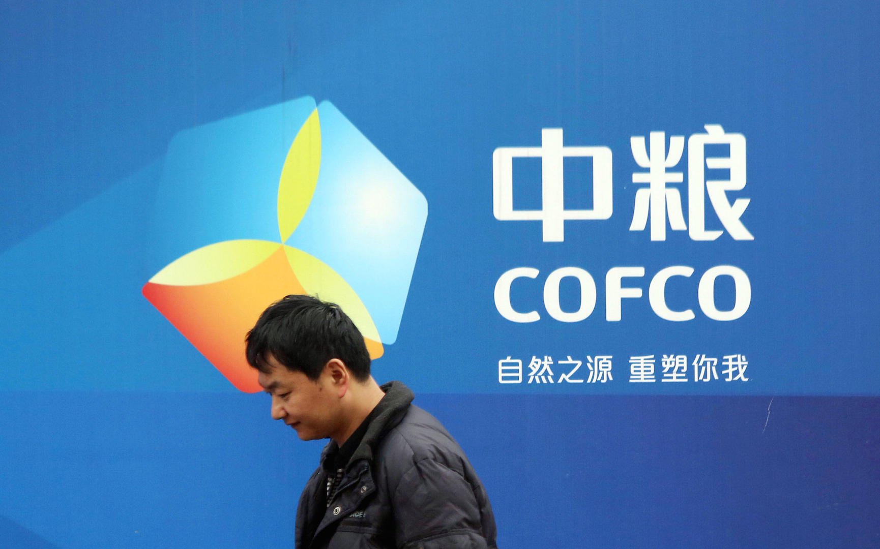 Um chinês em pé ao lado de um pôster da Cofco