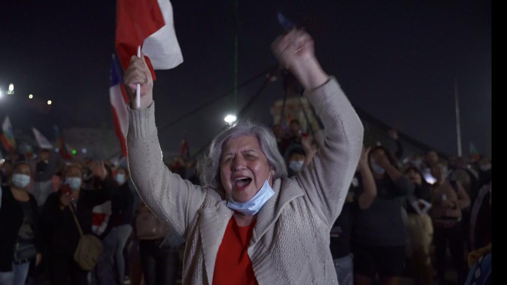 A woman celebrates in the street with the Chilean flag in her hand.
