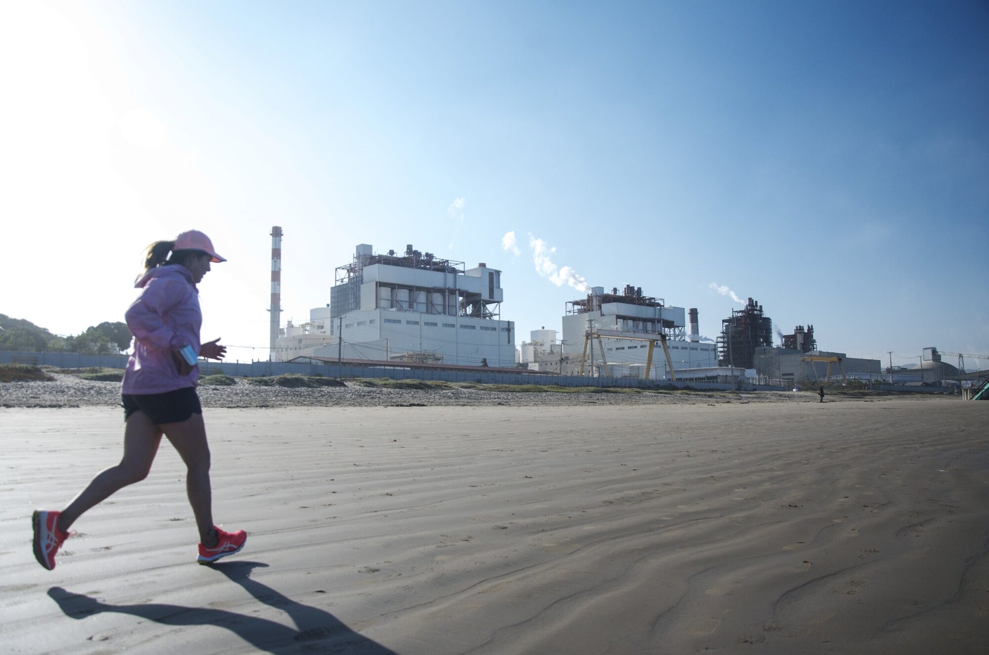 Mujer hace ejercicio en la playa, con el parque industrial de fondo