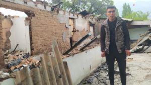 <p>Mirlan Piridin, 26, stands in front of the destroyed house where he lived with his parents, in the border village Ak-Sai, Batken region, Kyrgyzstan. Hours before the house was destroyed by an artillery shell, the family managed to evacuate (Image: The Third Pole)</p>