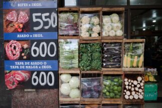 Cartel con precios de cortes de carne y cajones con verduras