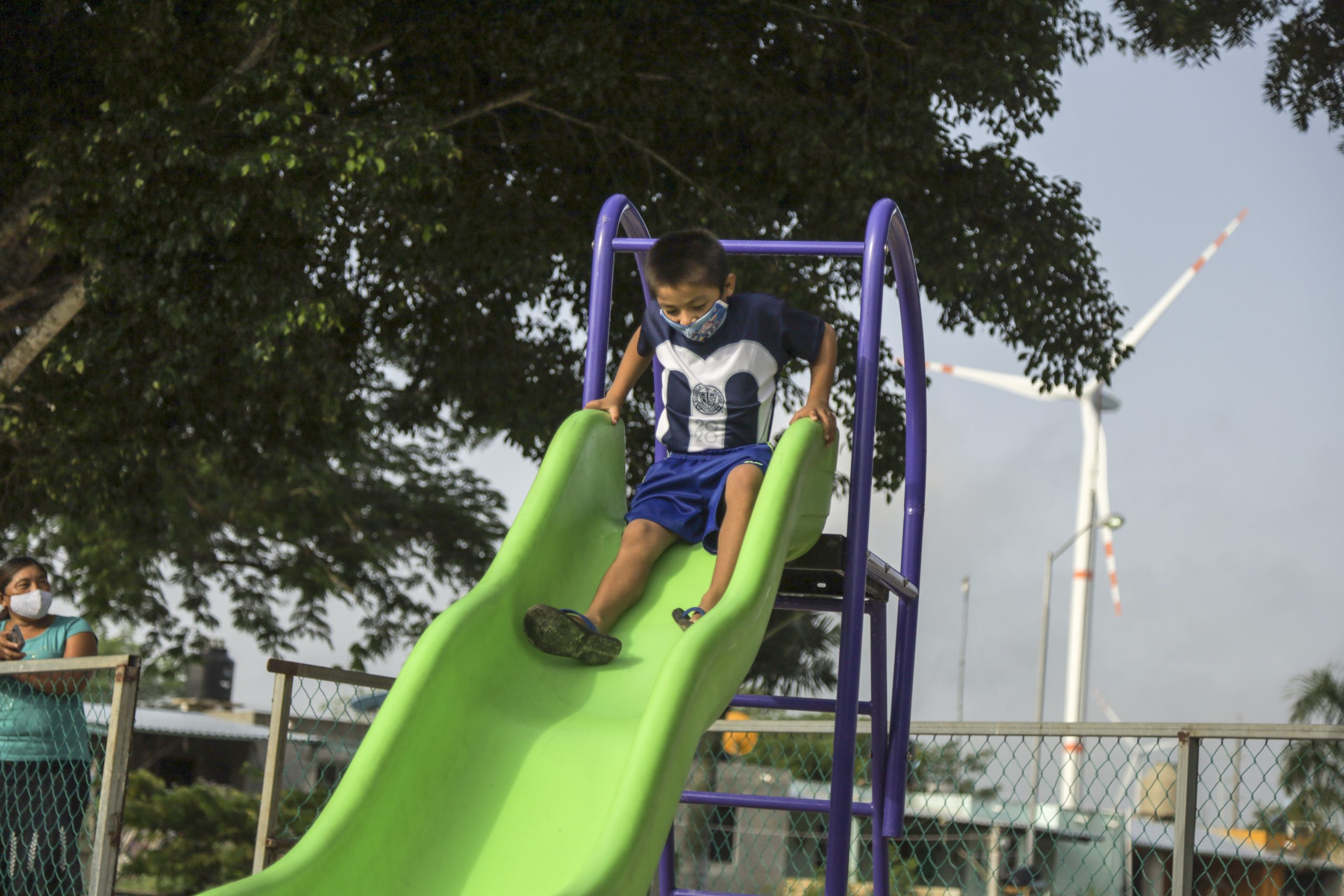 Uma criança brinca em um parque ao lado de um parque eólico.