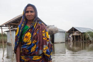 <p>A Bangladeshi woman stands in front of flooded buildings in 2019. Research indicates that women, children and the elderly are most vulnerable to poor mental health after disasters. (Image: Md. Rakibul Hasan / Alamy)</p>