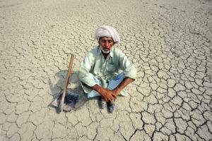 A farmer in Punjab, Pakistan, sits on the dry soil. More severe and frequent droughts are making it harder for people to grow crops where they have traditionally farmed.