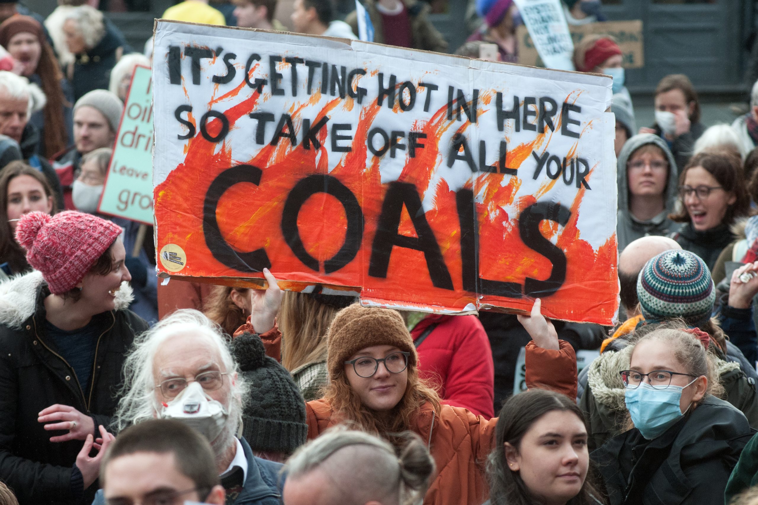 Demonstrators, one of them holding a sign saying "It's getting hot in here so take off all your coals".