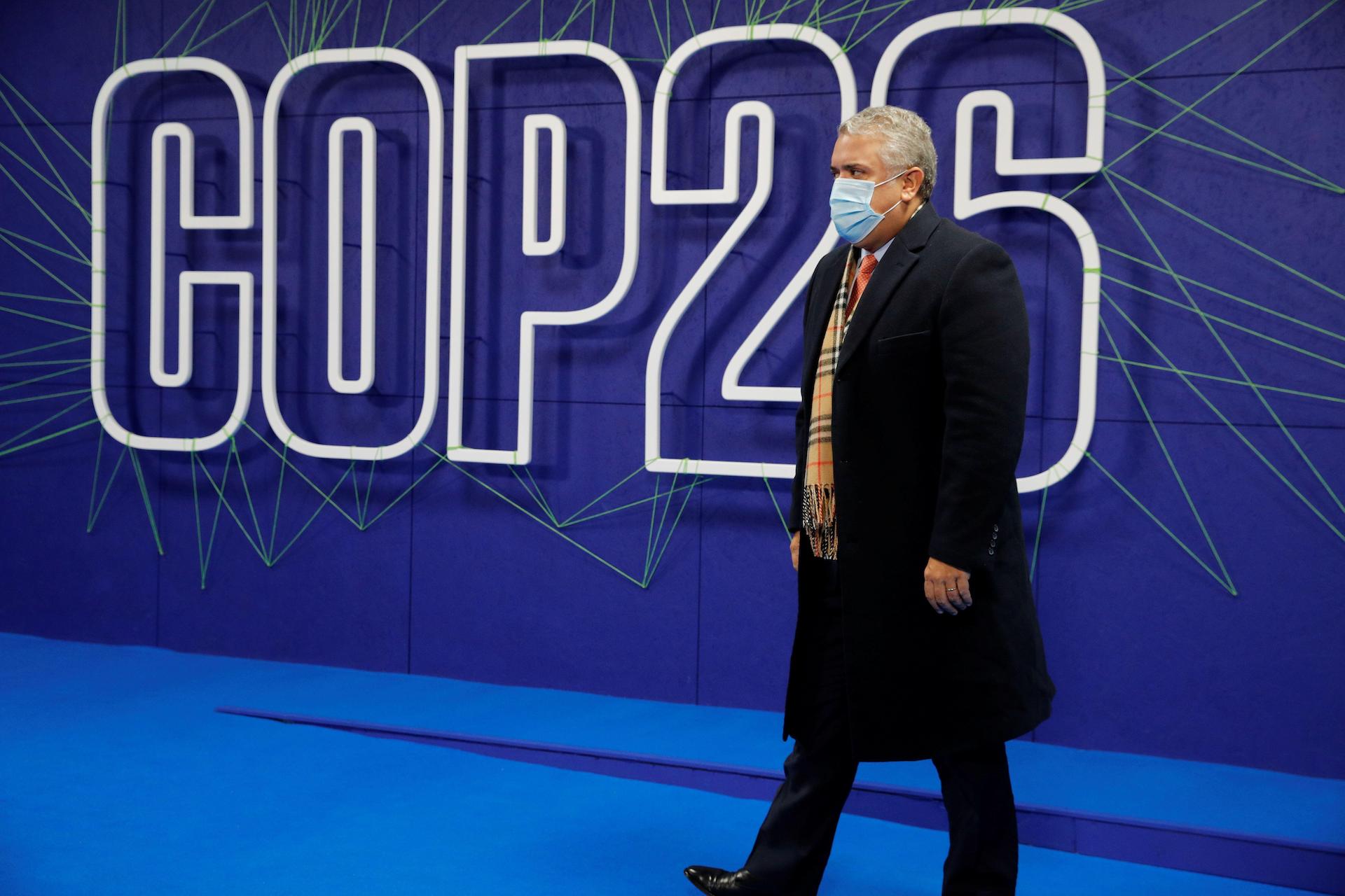 Ivan Duque caminha em frente a um pôster da COP26