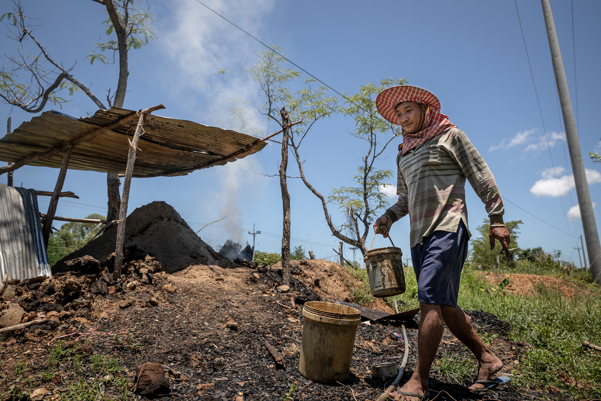 Farmer carrying a bucket of mud in front of a earth-mound charcoal kiln