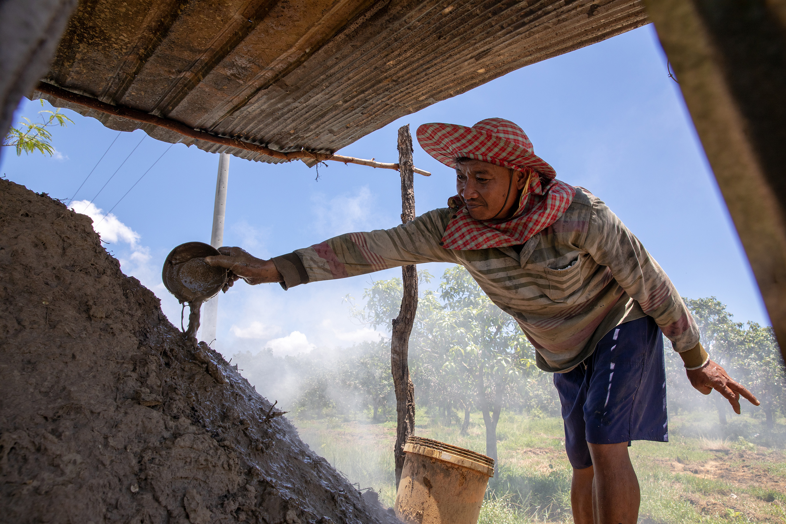Sokha adds mud to his earth-mound kiln to stop the smoke escaping.