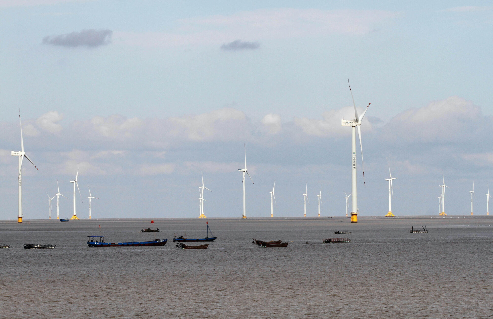 <p>Fishing boats pass a wind farm in Jiangsu province. China is exploring the potential of turning wind turbine bases into “marine ranches”, where seafood can be harvested for human consumption. (Image: Alamy)</p>