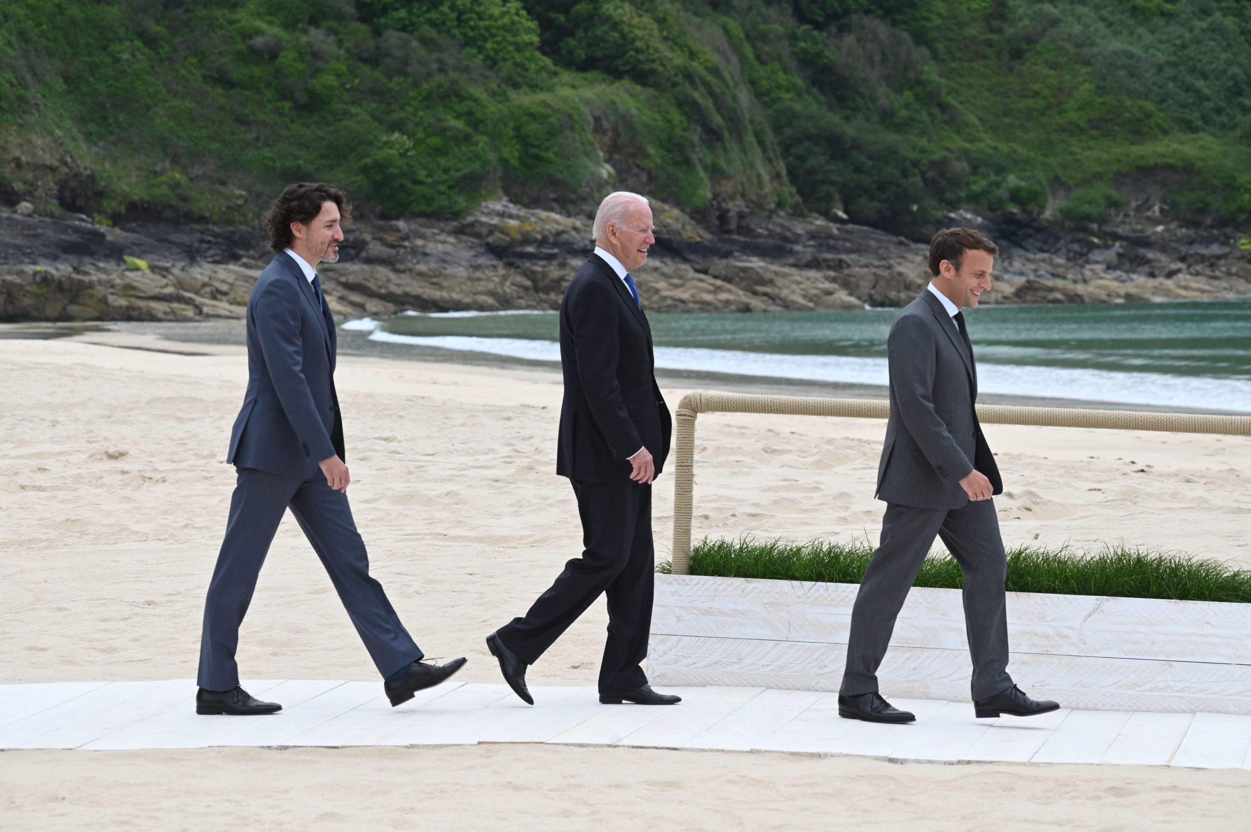 Trudeau, Biden e Macron caminham em uma praia