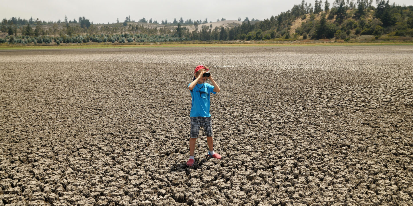 Criança no deserto olhando com binóculos.