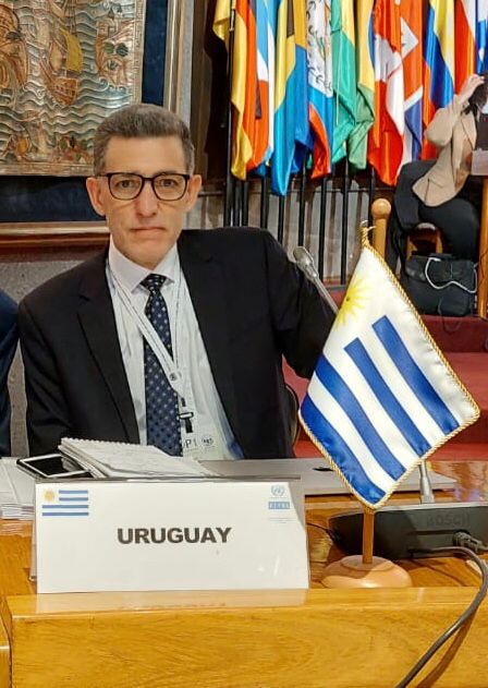 Un hombre detrás de un escritorio con la bandera de Uruguay un cartel que dice "Uruguay"