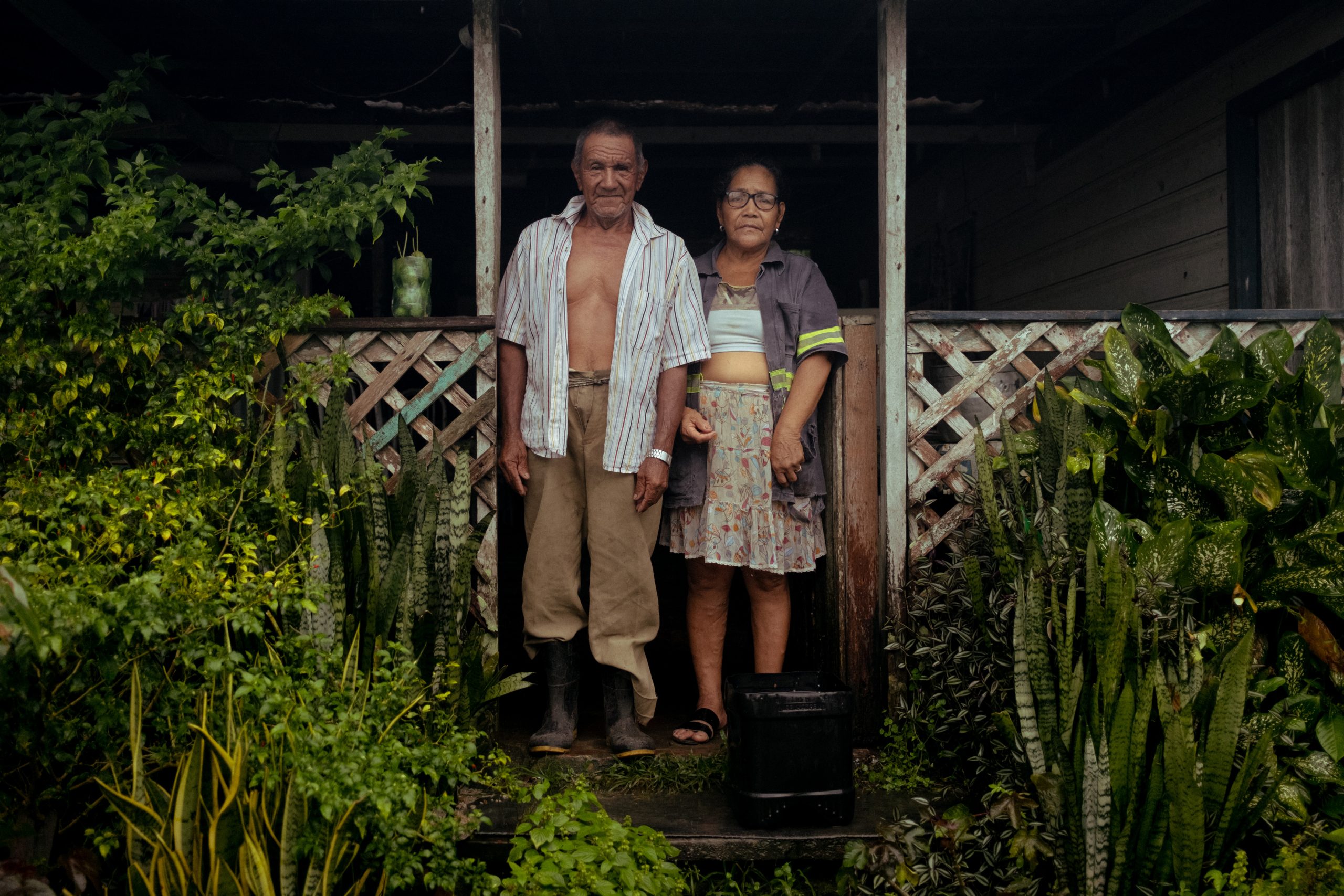 Um homem e uma mulher na porta de sua casa, com plantas em ambos os lados.