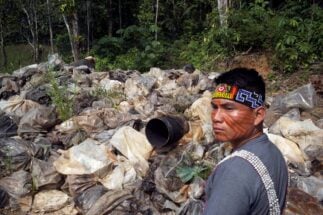 membro de uma comunidade indígena ao lado de sacos de lixo