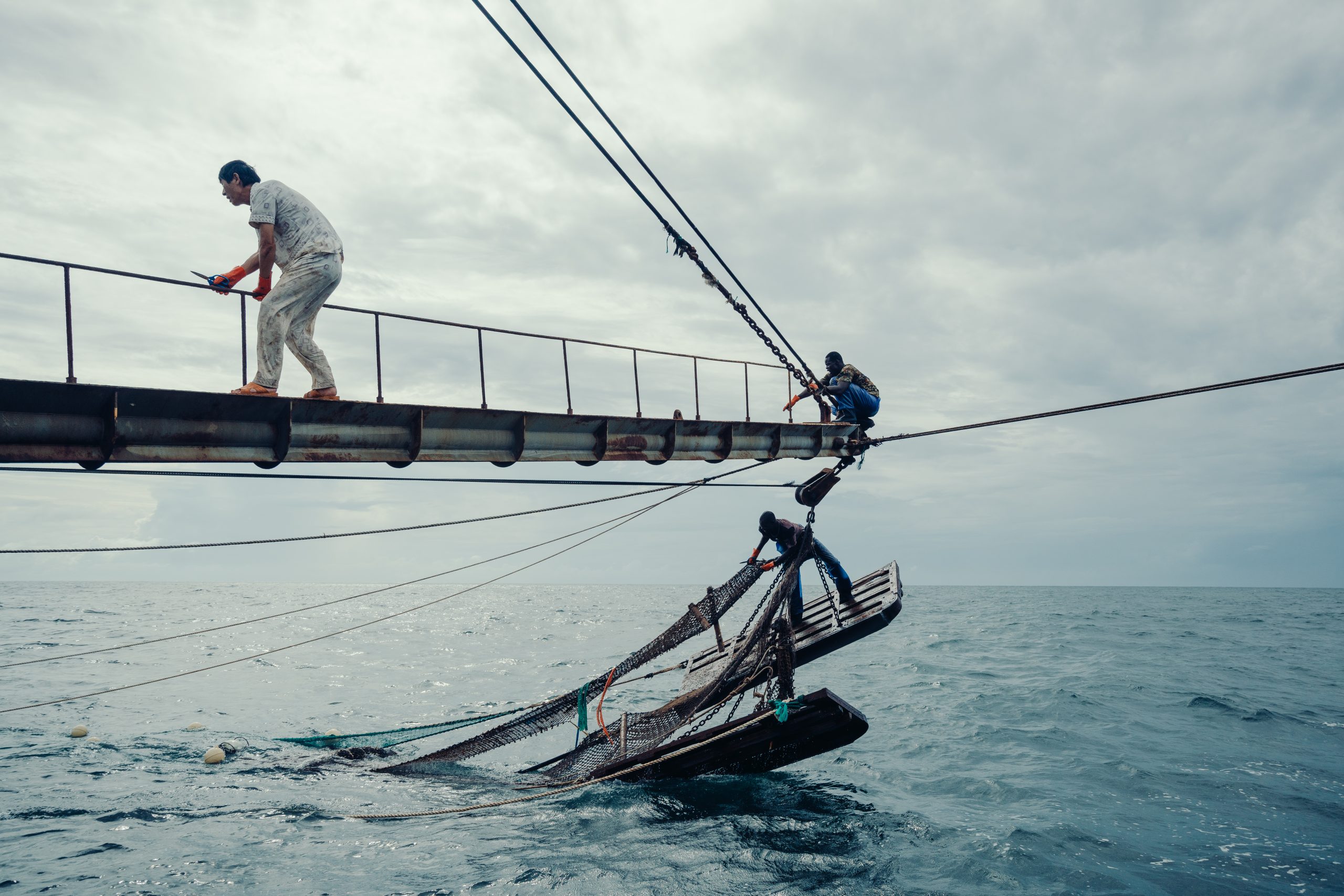 <p>A Chinese fishing vessel in the waters of Guinea-Bissau. The captain (left) and two local sailors (right) are trying to release a trapped net. (Image: © Liu Yuyang / Greenpeace)</p>