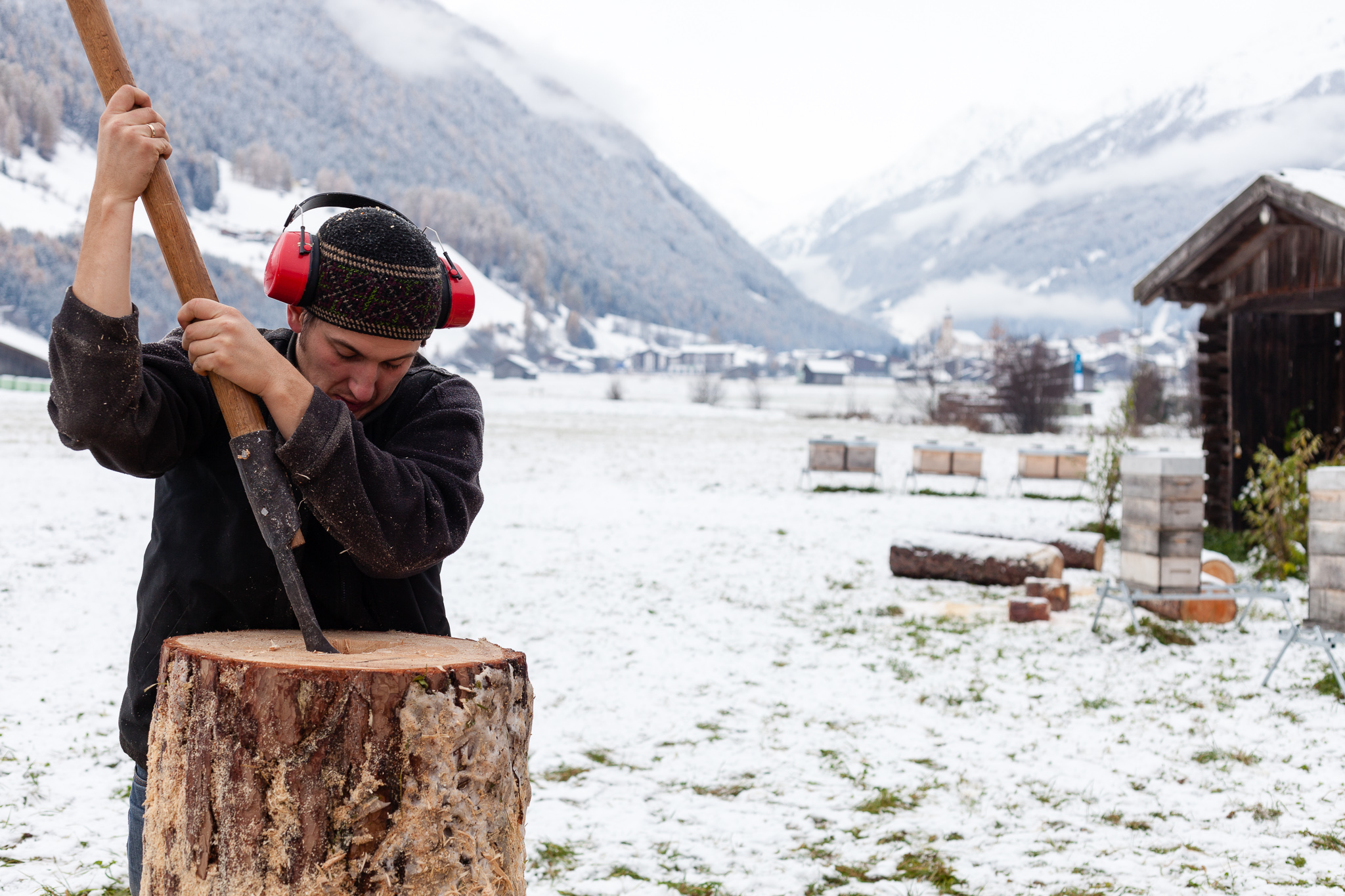 Piotr Piłasiewicz uses a gouge to hollow out a log hive, with a snowy field and mountains in the background