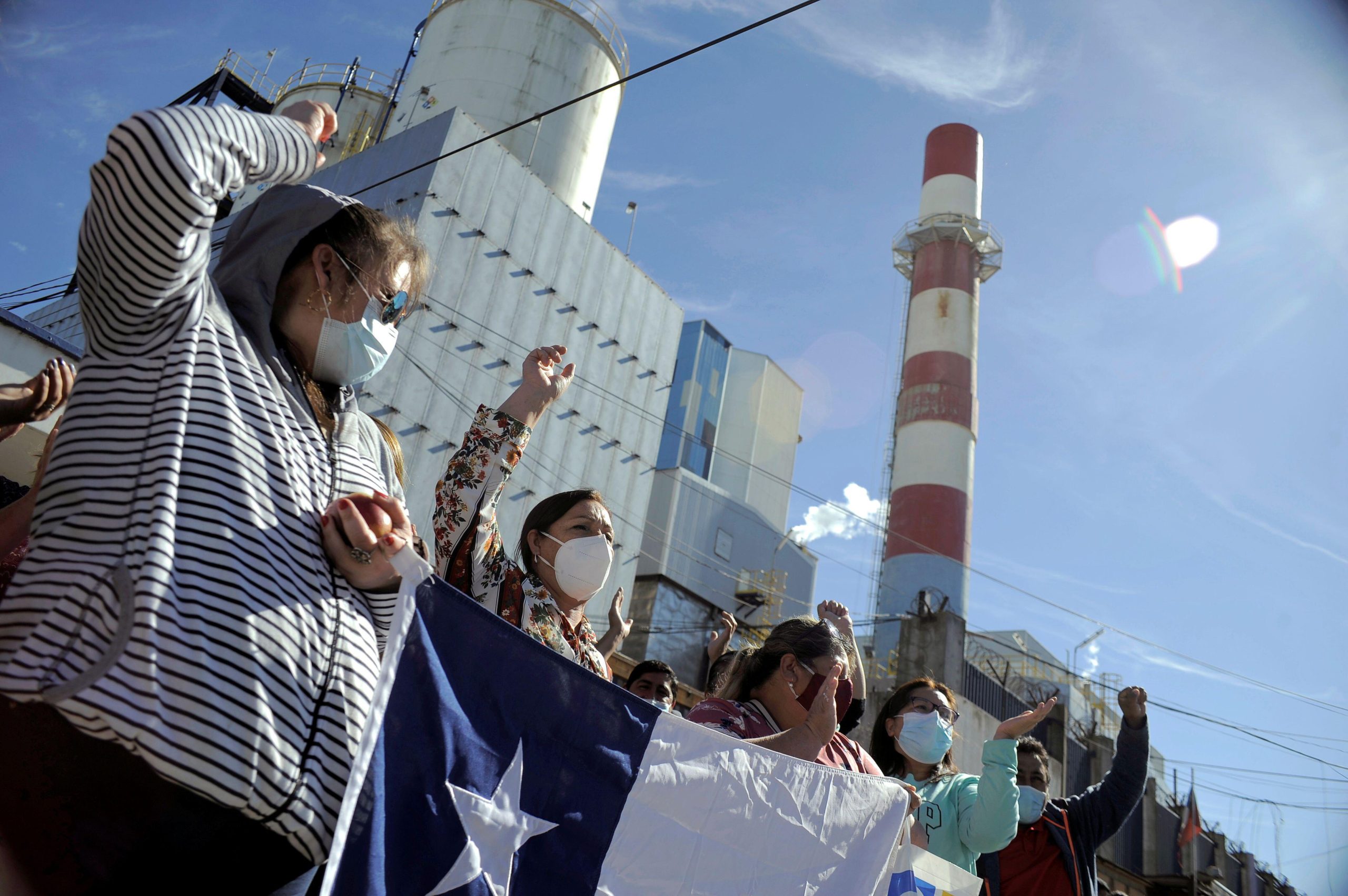 demonstrators holding a Chilean flag in front of a thermoelectric power station