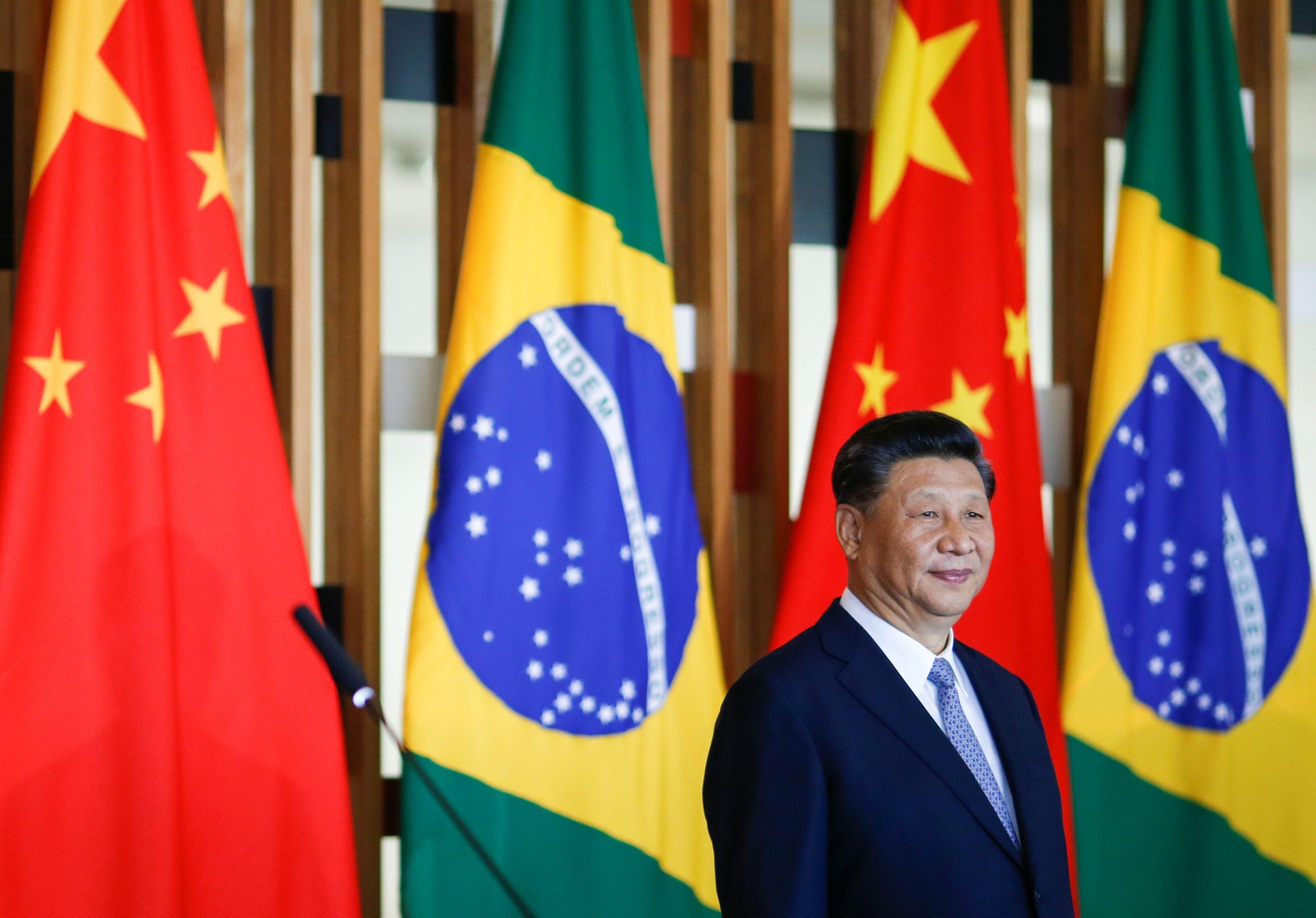 Xi Jinping em um evento com bandeiras do Brasil e da China atrás dele