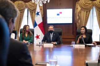 personas sentadas alrededor de una mesa con barbijos. Detrás de la mesa hay una bandera de Panamá