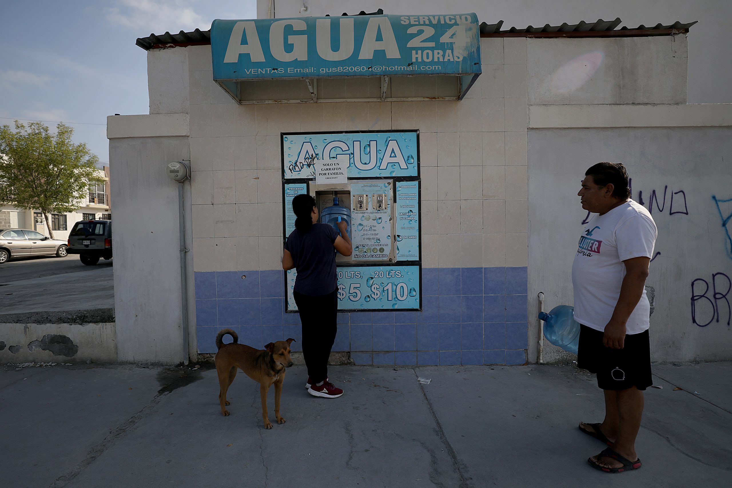 A woman buys water from a stall with a sign saying "24-hour water".