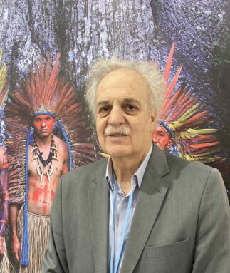 Carlos Nobre em frente a uma foto de membros de uma comunidade indígena