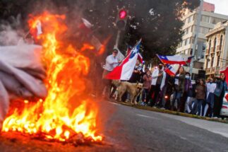 Una pancarta es incendiada mientras manifestantes sostienen banderas chilenas durante una protesta contra la nueva Constitución en Valparaíso.