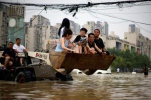 People ride on a front loader as they make their way through floodwaters following heavy rainfall in Zhengzhou, Henan province, China July 23