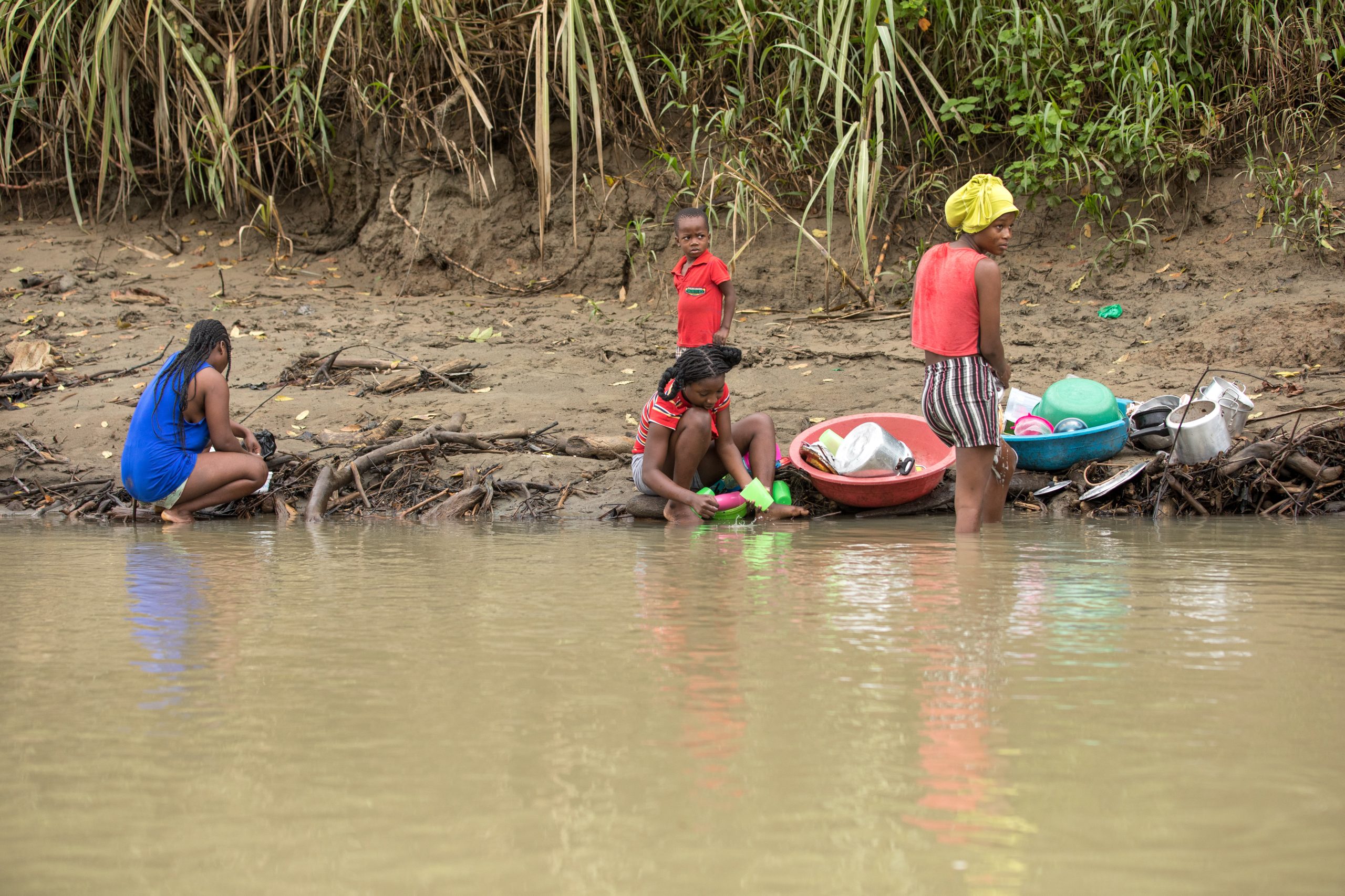 small group of women and children sitting on river bank washing dishes 