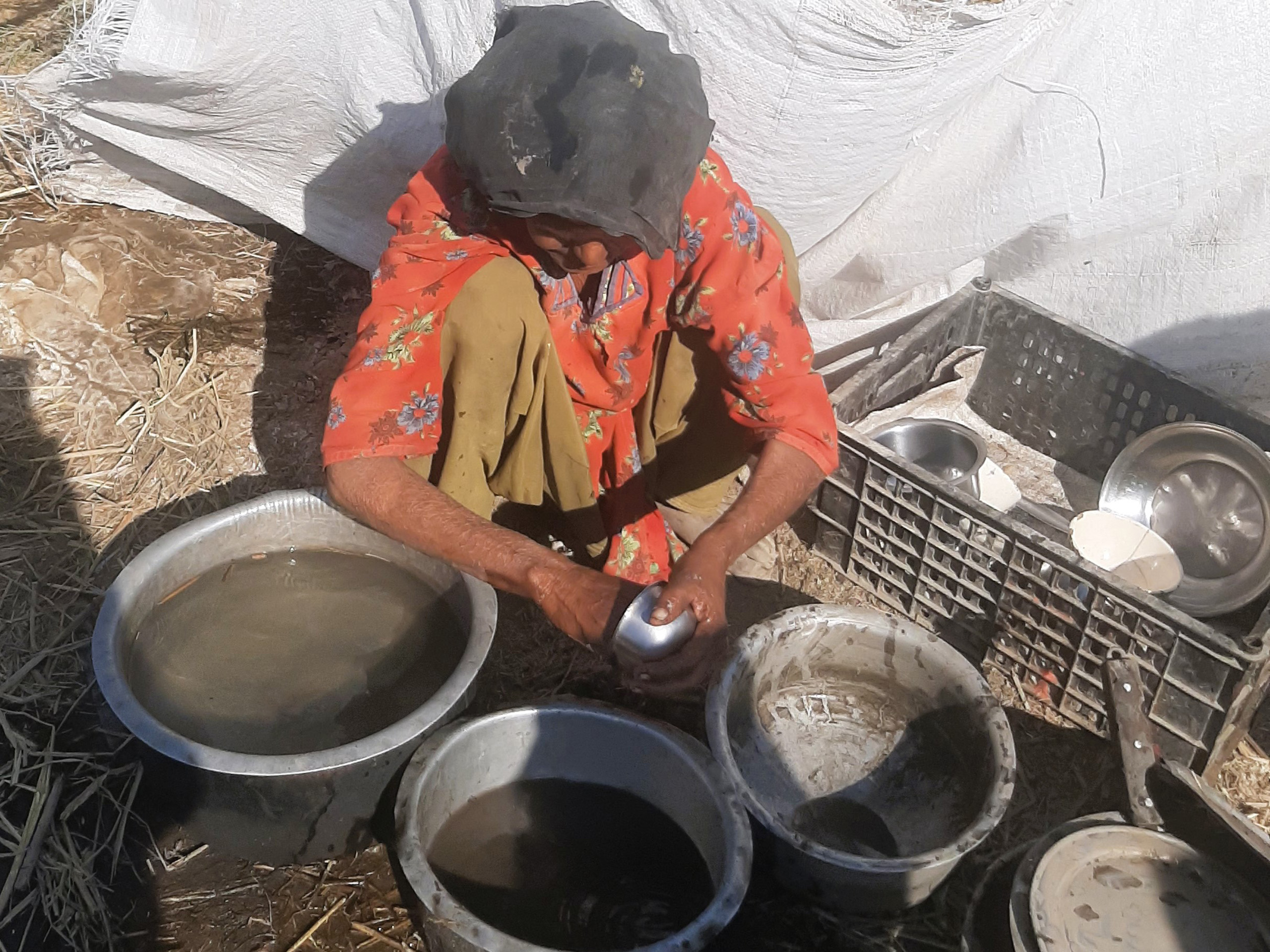 A women in Pakistan sits next to bowls used for carrying water