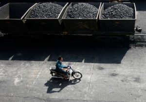 A worker rides his motorcycle near lorries transporting coal in Vietnam