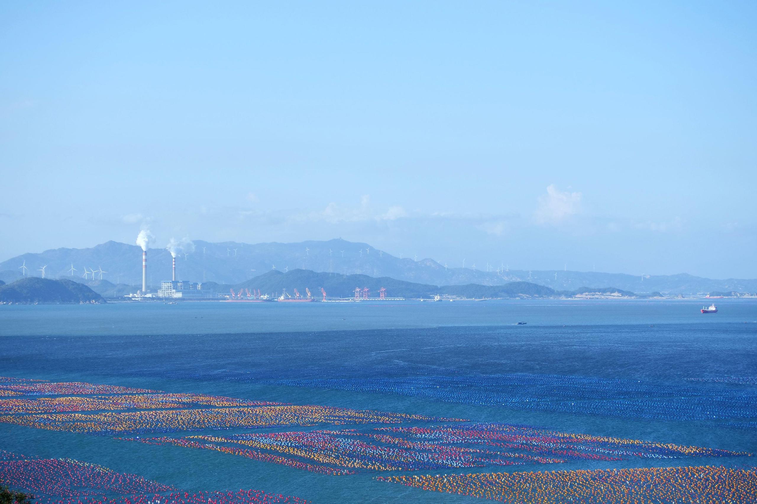Blue coastal view, Guangdong China, oyster farm on ocean surface with smokestacks from coal power station in background
