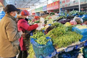 People shop for vegetables at a vendor in a food market in Shanghai