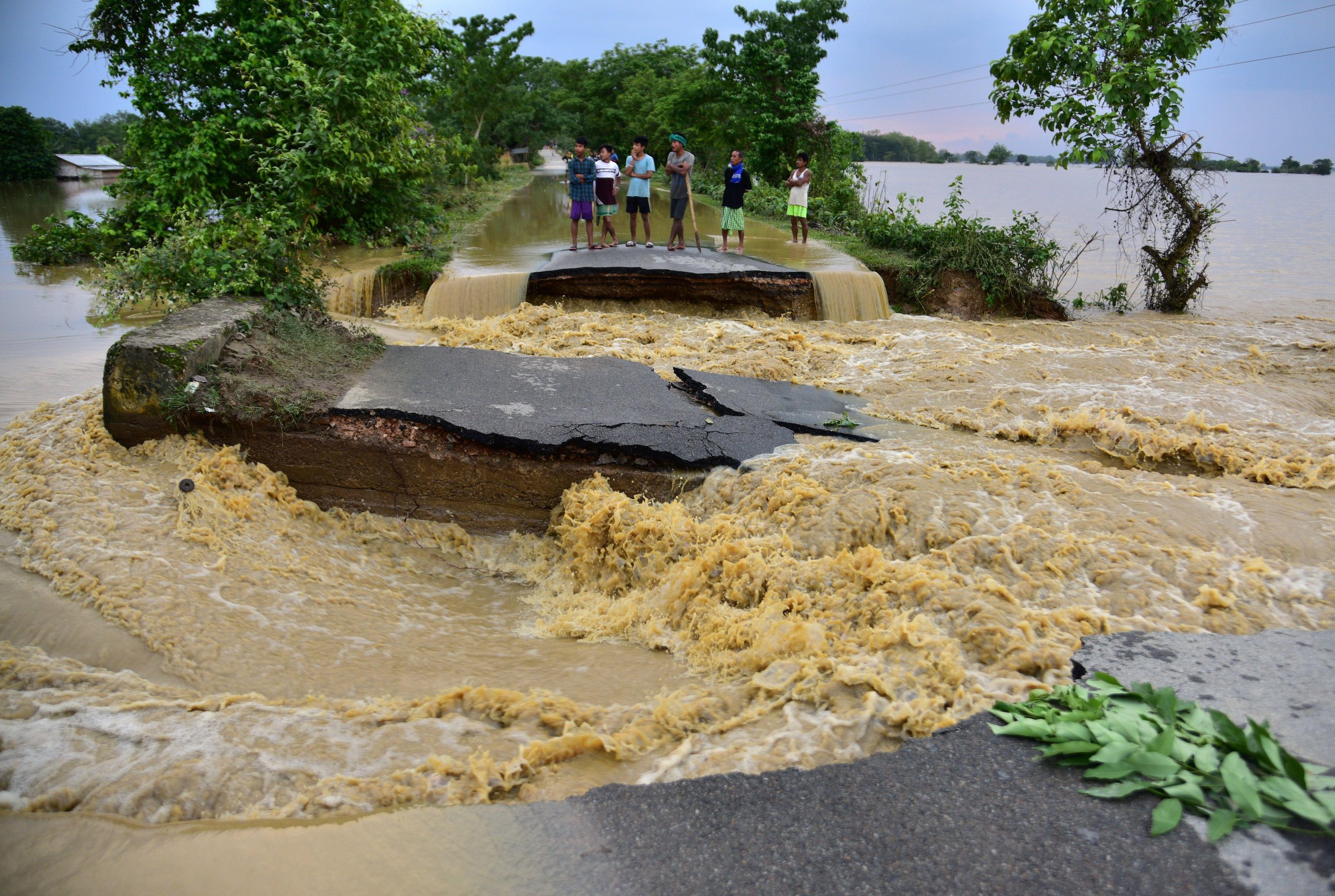 People stand on a road damaged by flooding in Nagaon district, Assam, India 
