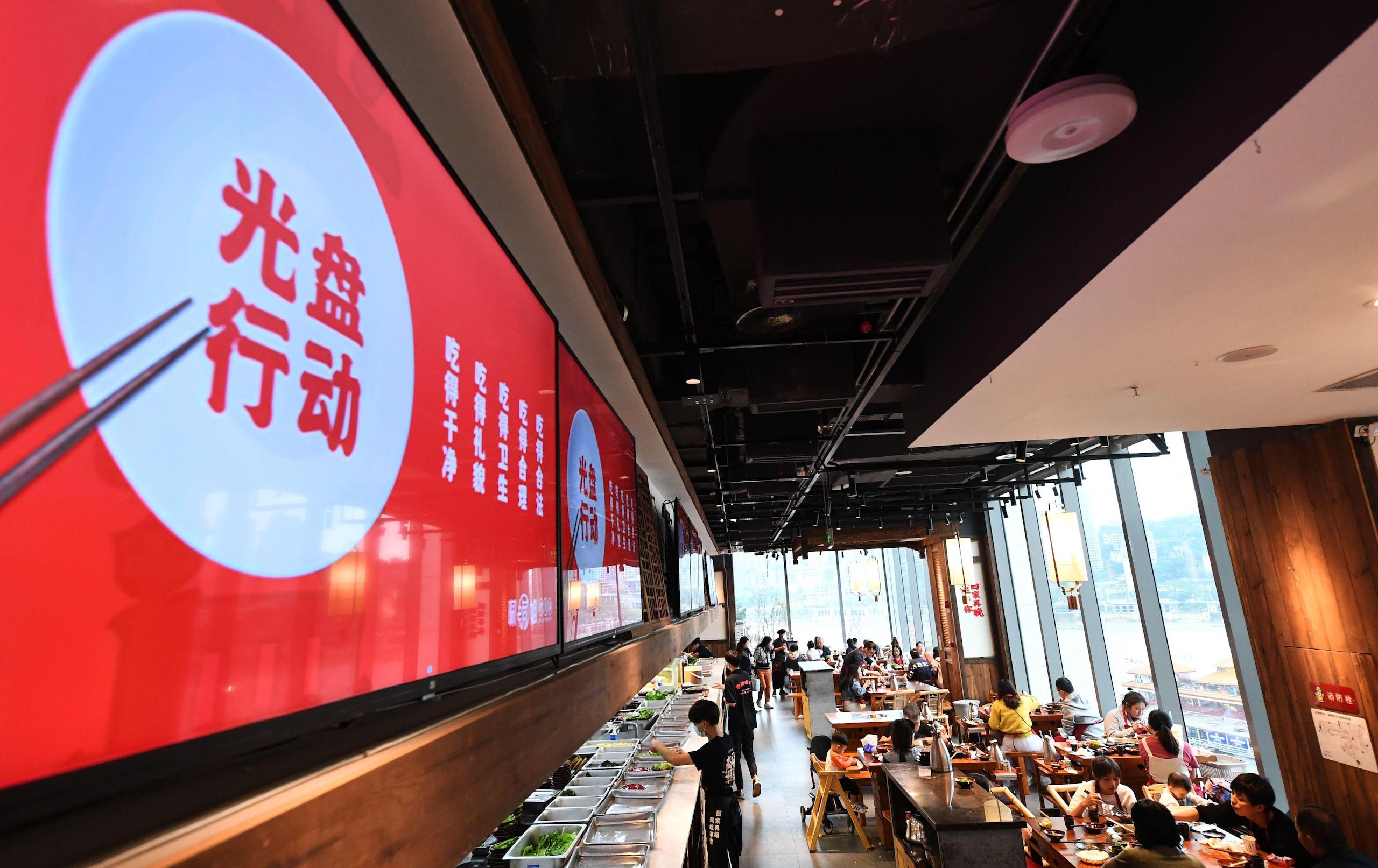 TV screens show "Clear Your Plate" campaign in a hotpot restaurant in  Chongqing, China