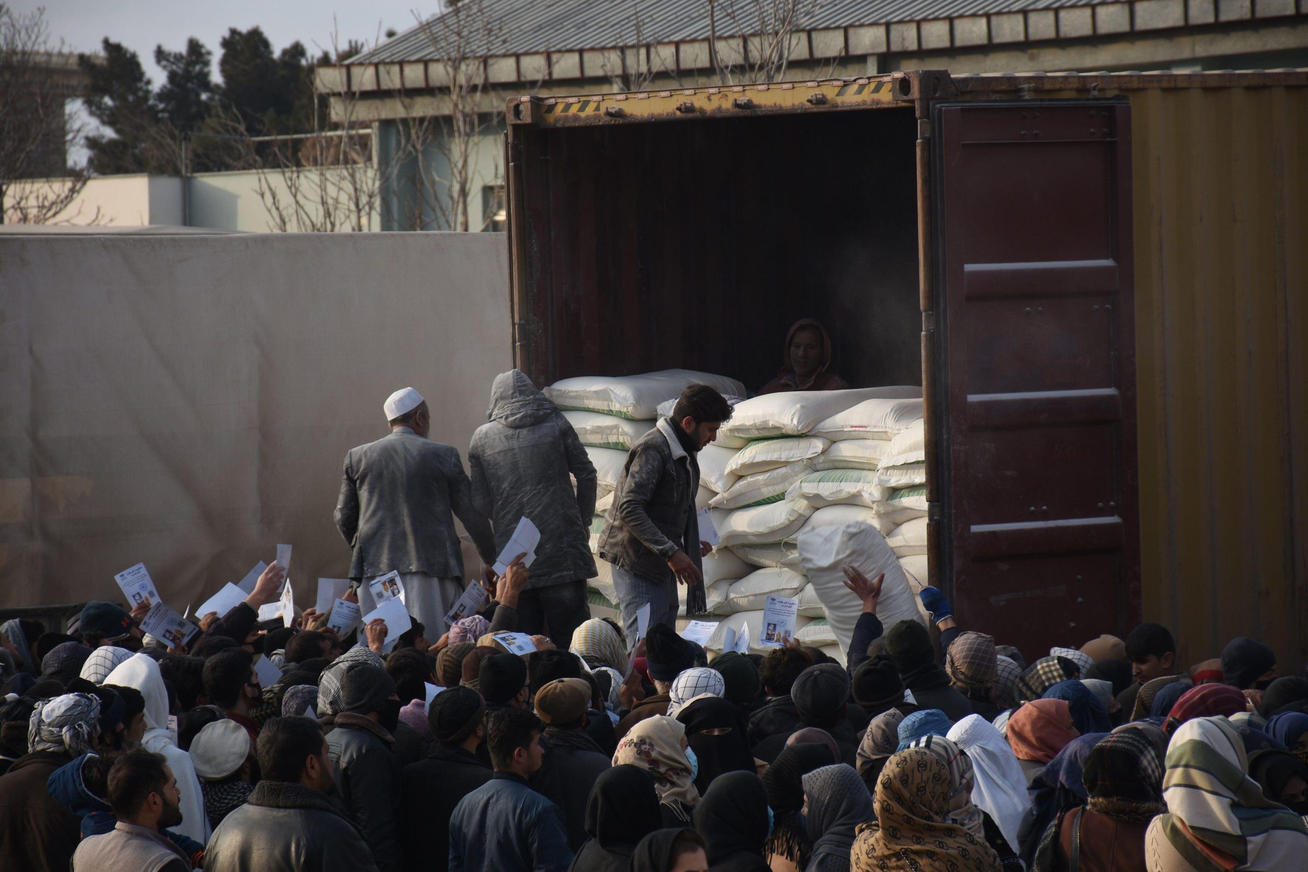 crowd of people below men unloading large sacks from back of truck