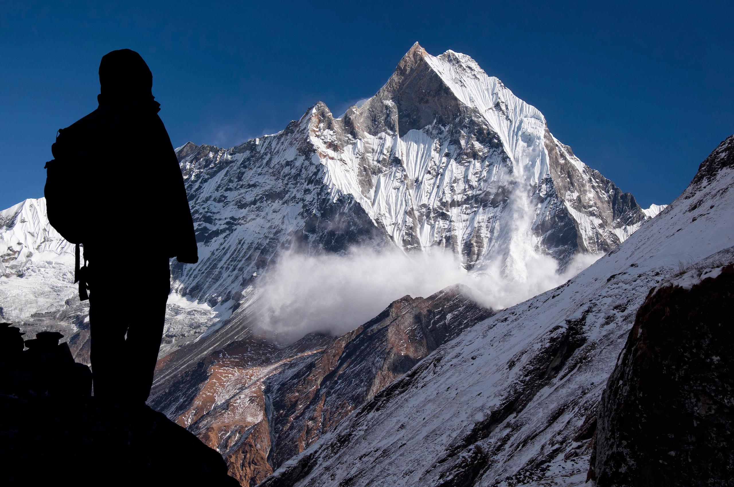 Annapurna region, avalanche on the holy Machapuchare mountain viewed from Annapurna Base Camp, silhouette of a trekker in the foreground
