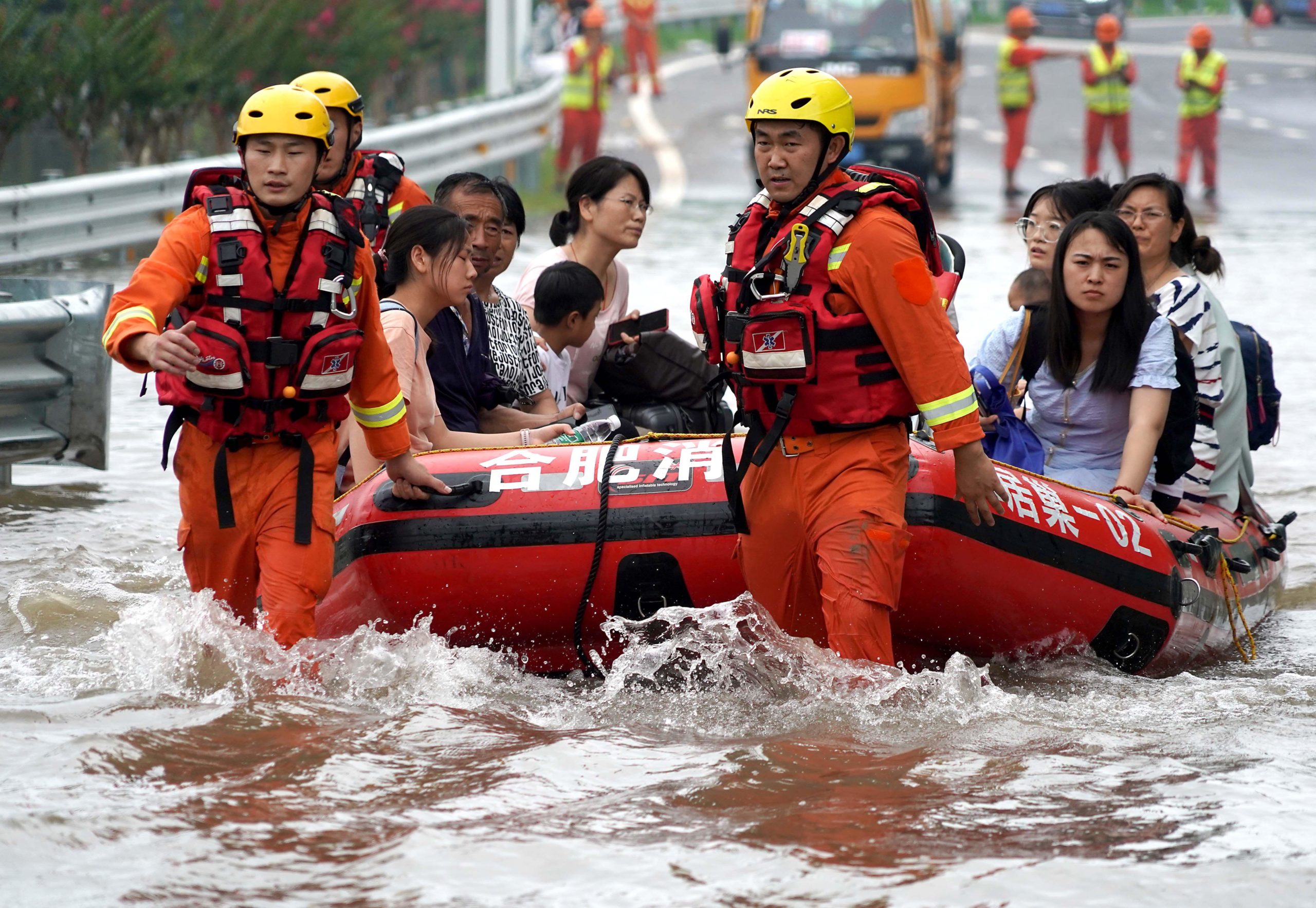 people on inflatable raft being pulled through flood water