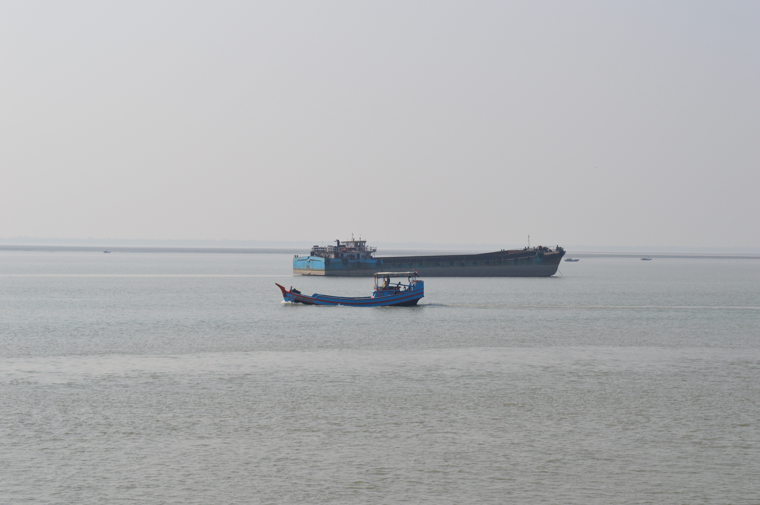 Barge passing a fishing boat on India Bangladesh transboundary river, misty view across Sundabans mangrove