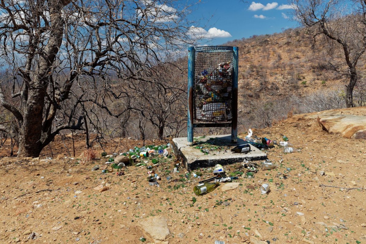 an overflowing bin with broken bottles surrounding it