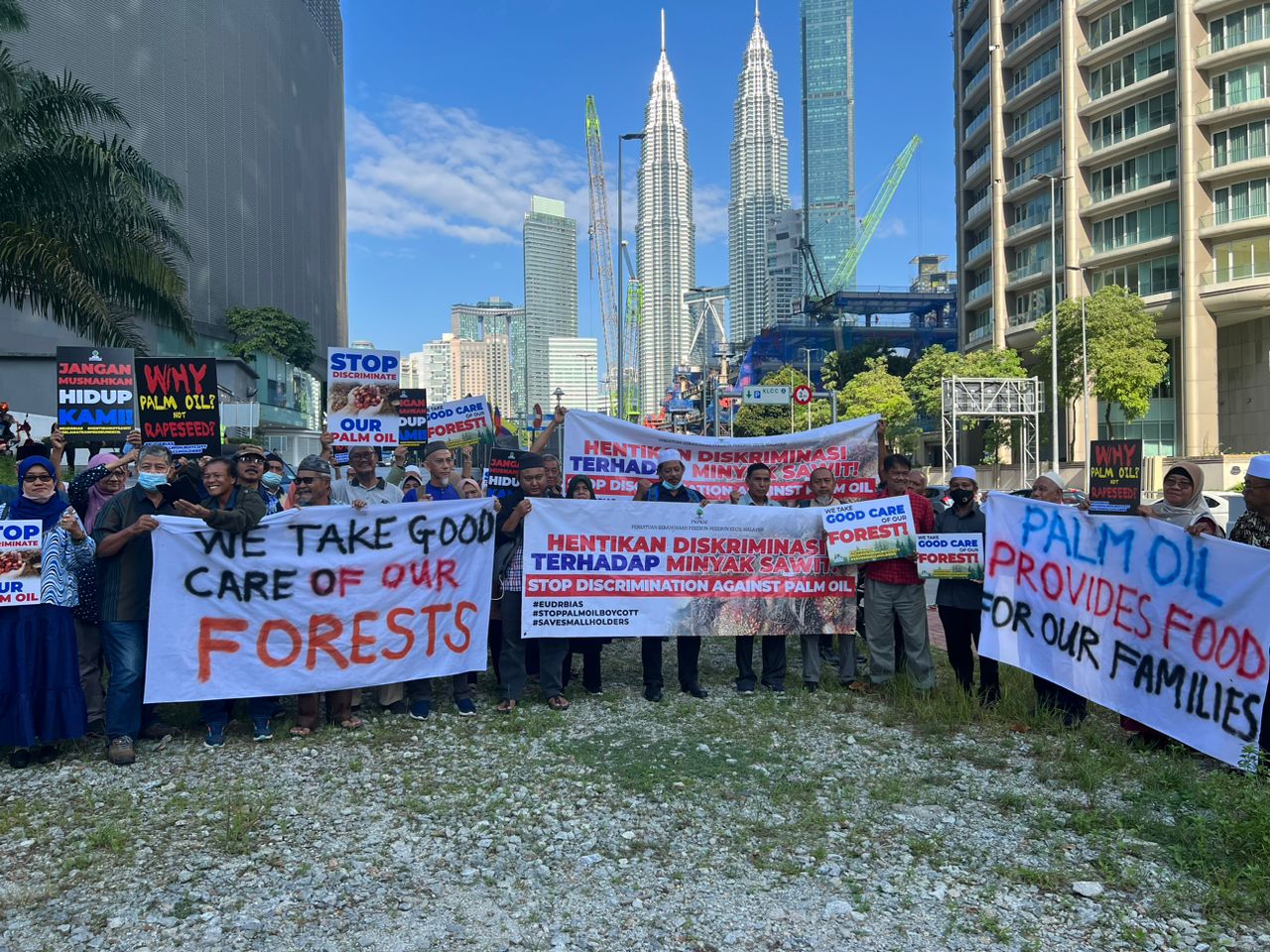 Group of Malaysian farmers gather in Kuala Lumpur, hold hand-painted placards, protest the EU Deforestation Regulation (EUDR), blue sky Petronas towers in the background