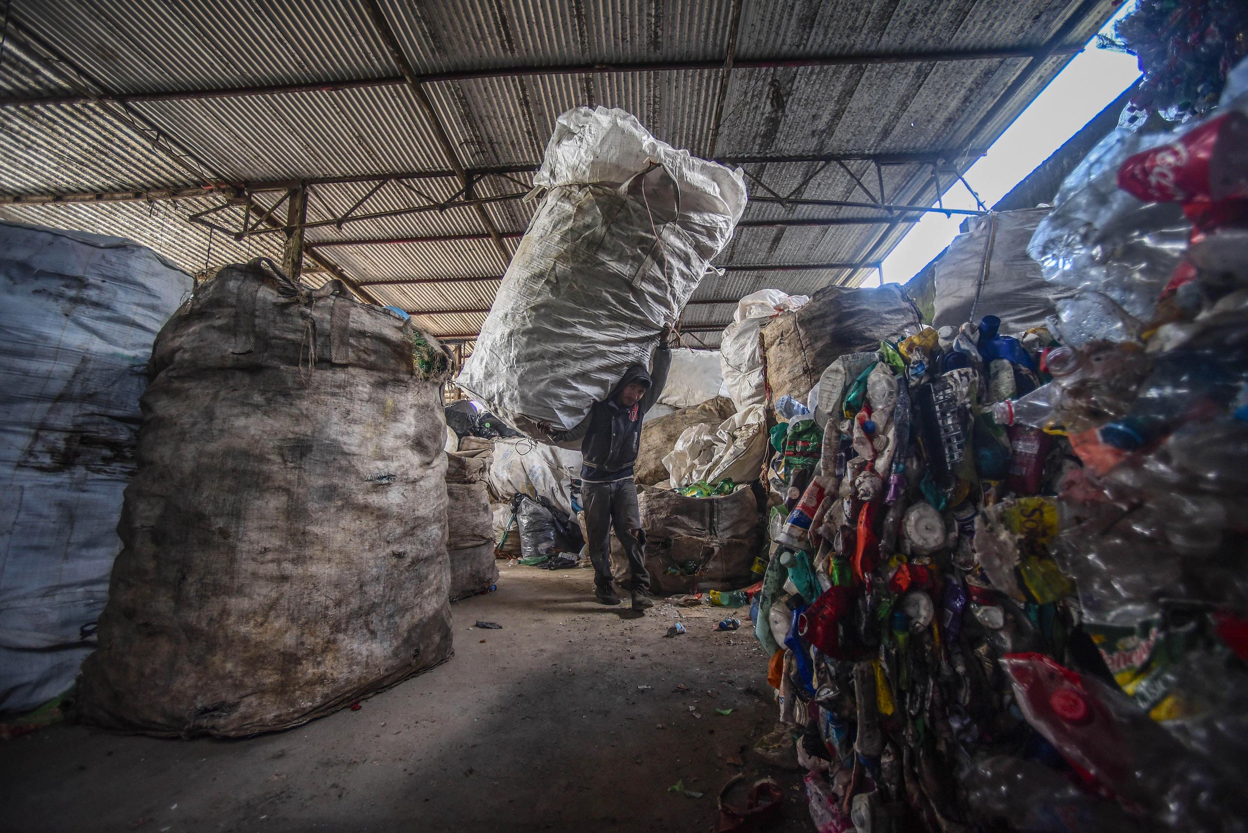 A waste pickers carries a giant bag of waste on his shoulder walking into a recycling plant in Mexico
