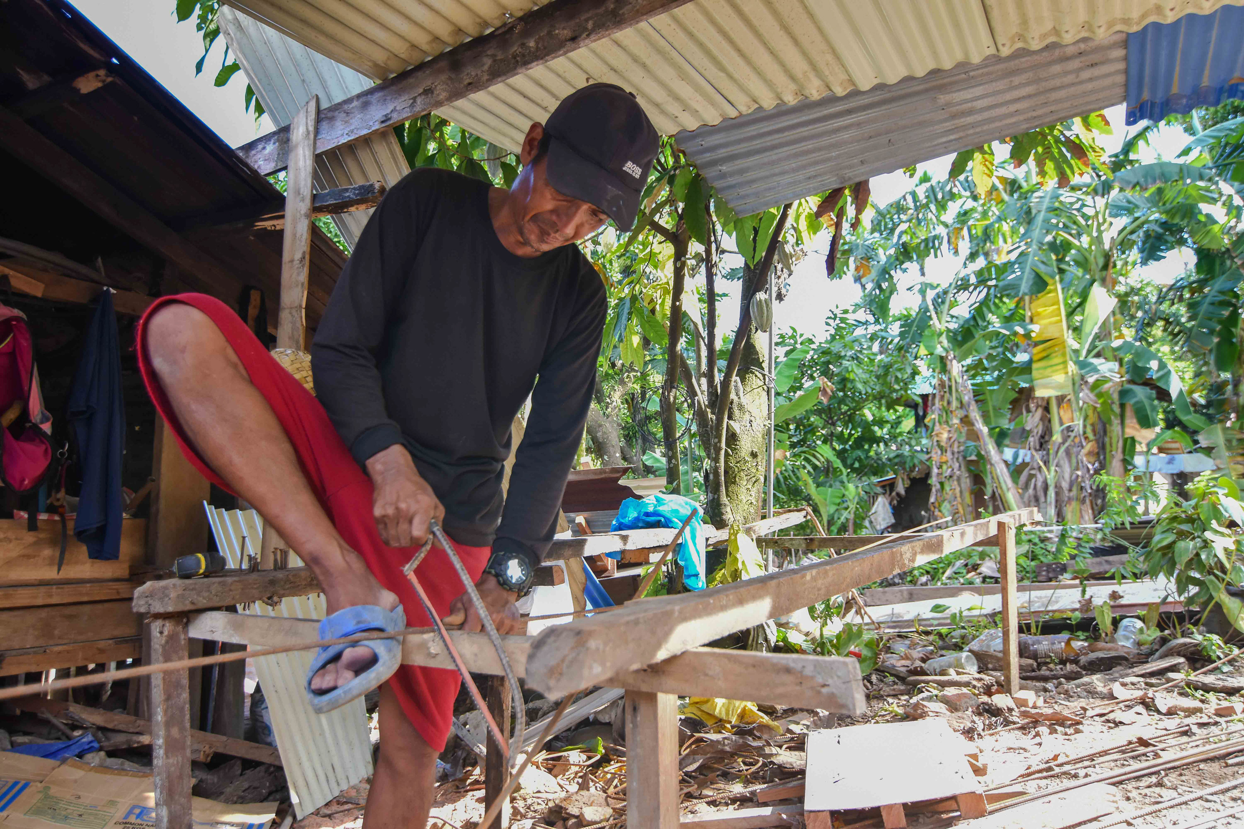 man using handsaw to cut long tube held in place by his foot